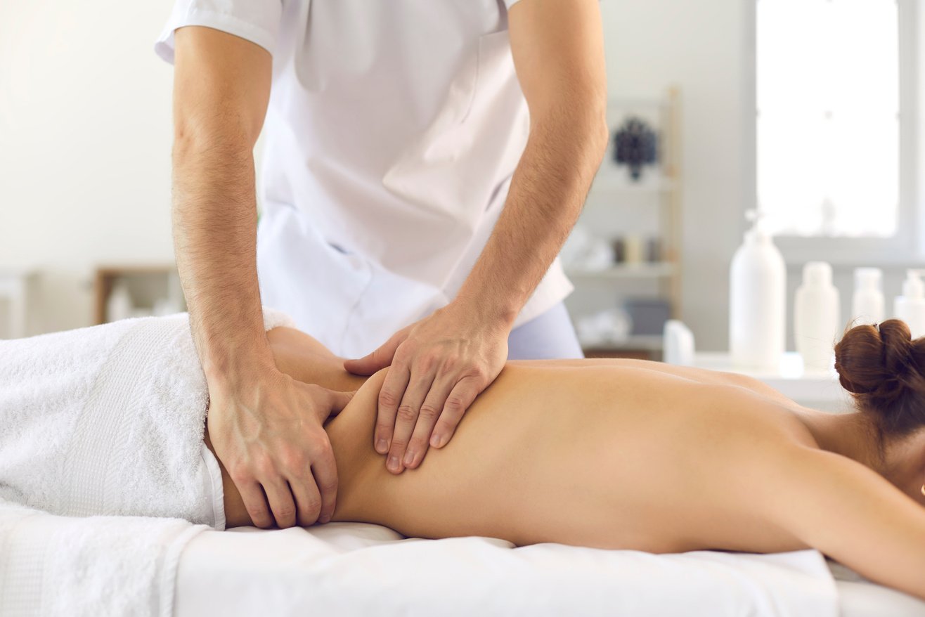 Male Osteopath Massages the Back of a Girl Lying on a Couch in a Bright Office.